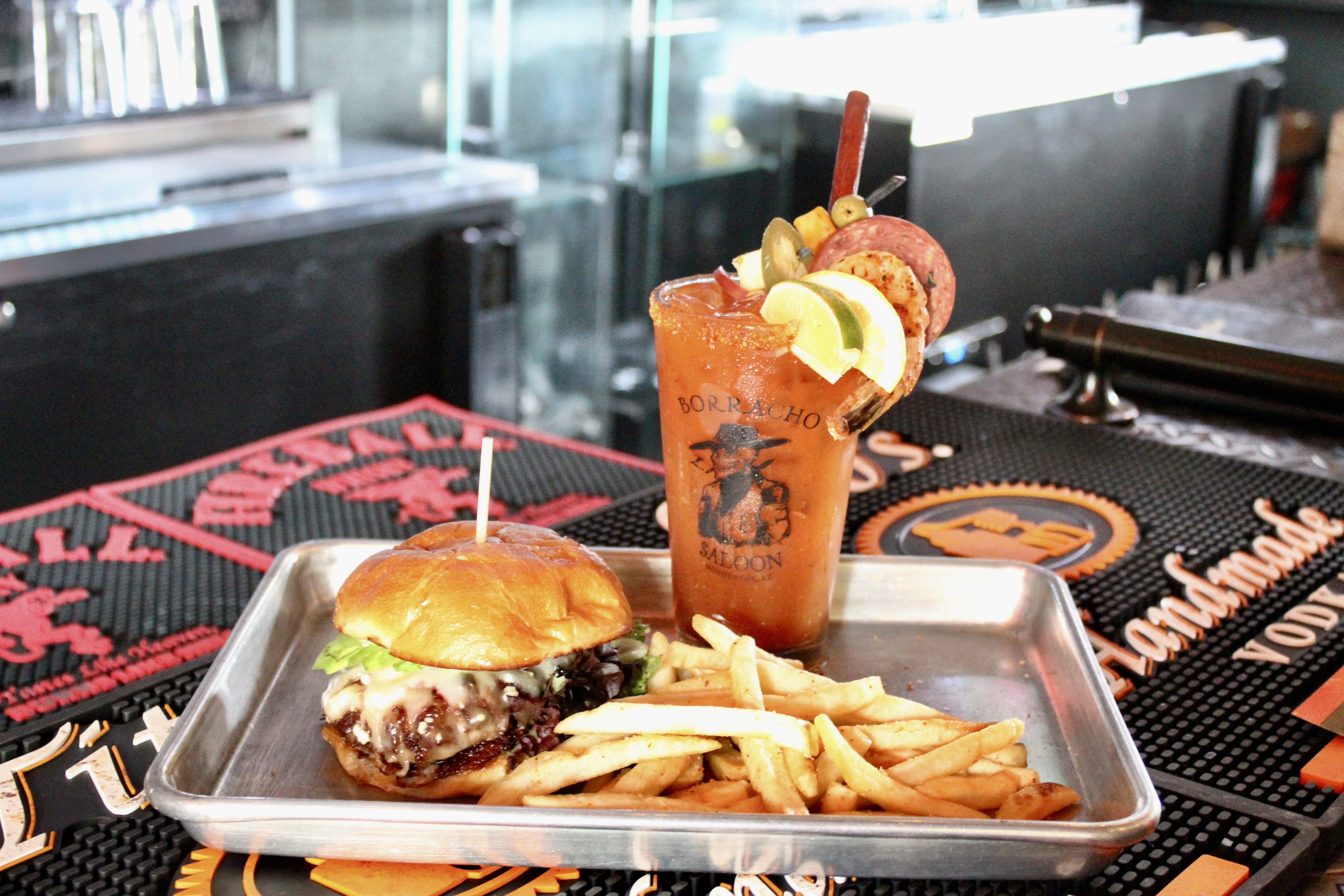 Borracho Saloon cheeseburger plated on a silver tray with fries and a Bloody Mary in a Borracho Saloon glass