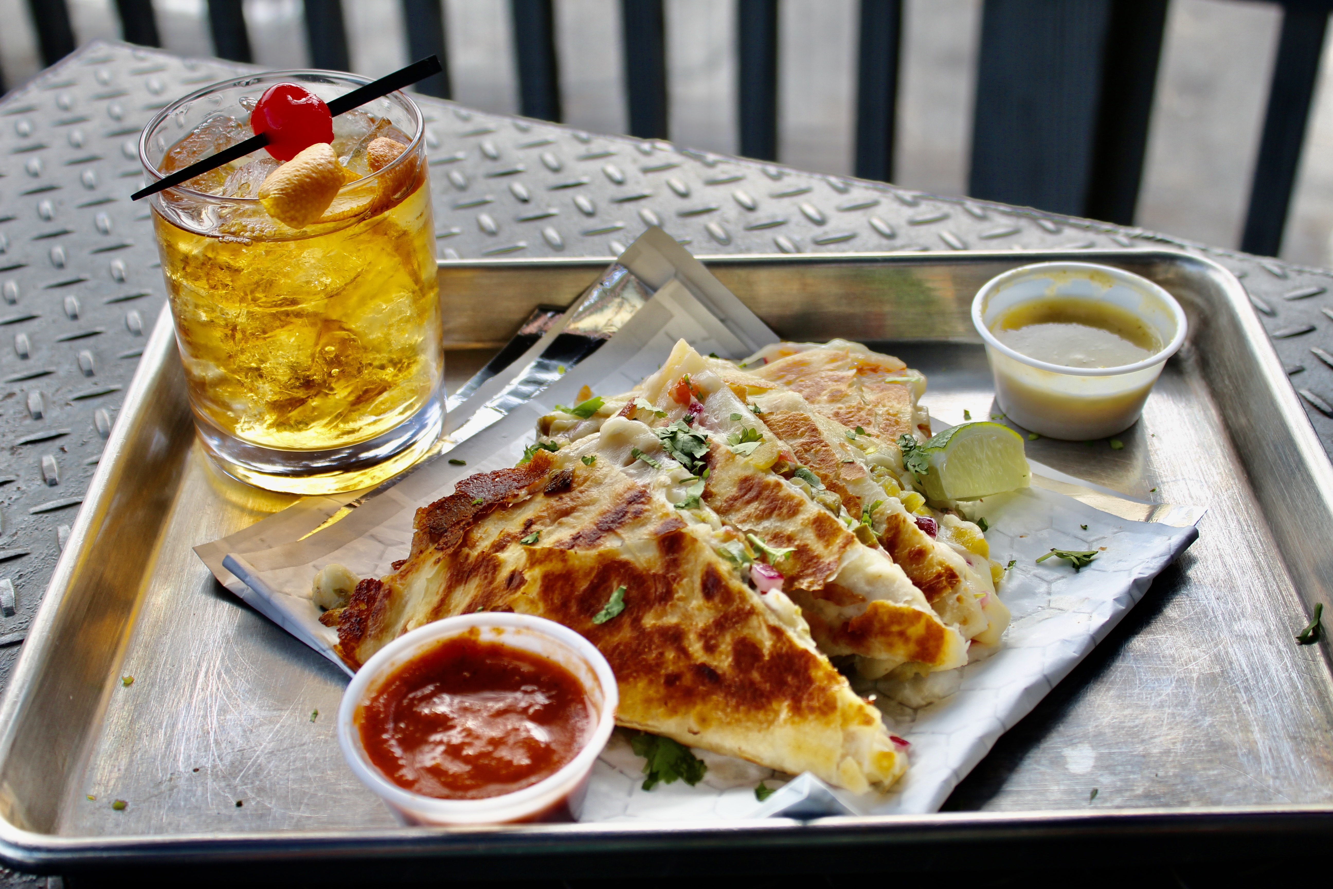 Borracho Saloon quesadillas plated on a silver tray with a red sauce, green sauce and Old Fashioned drink