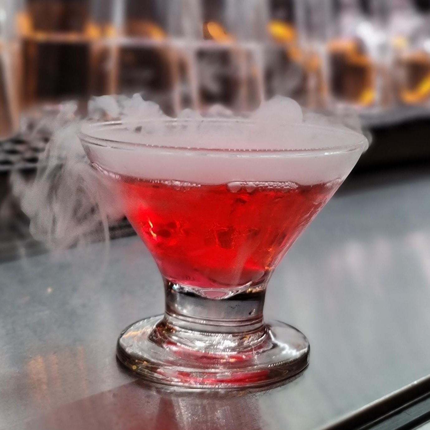 Red cocktail sitting on top of the bar counter with smoke coming out of the top