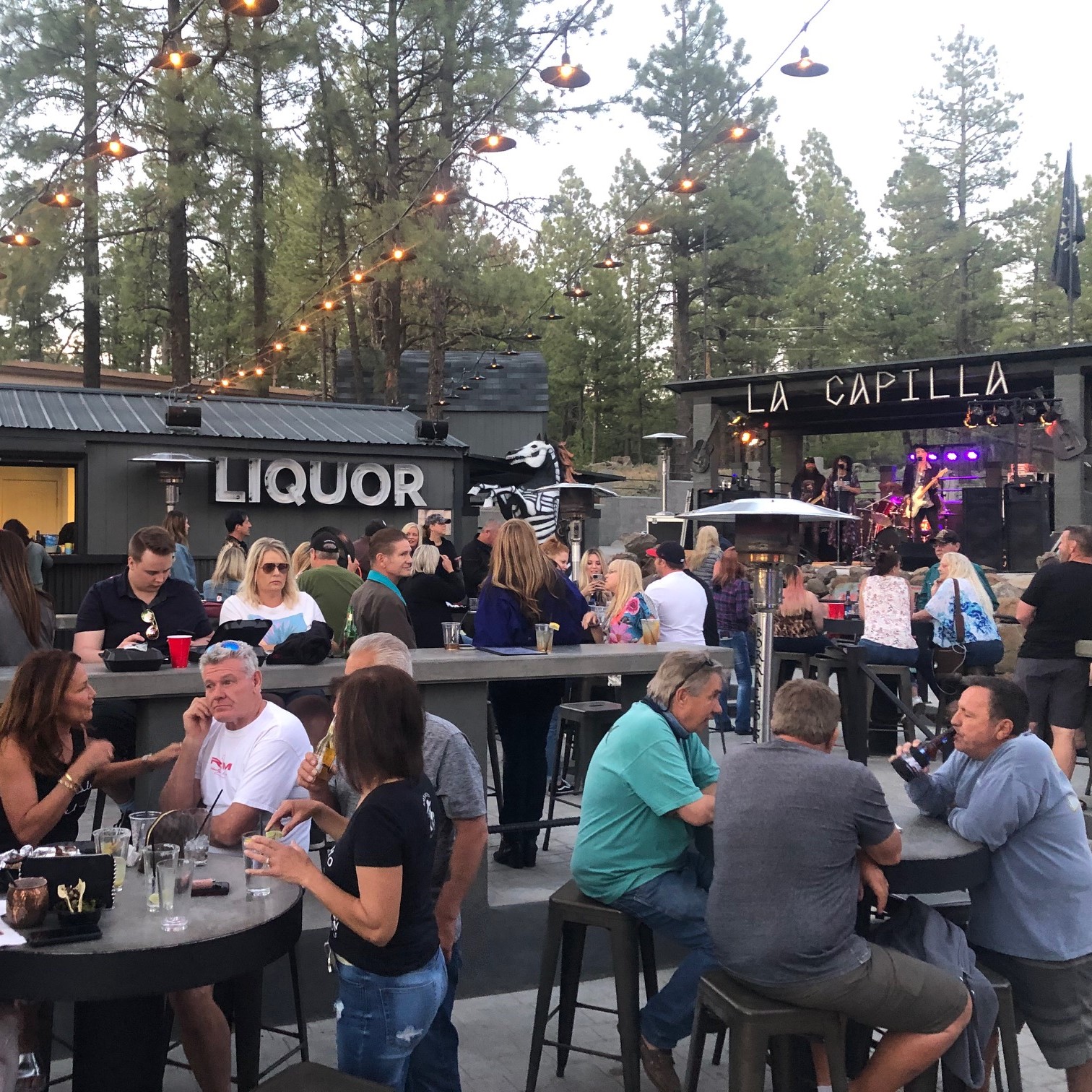 A filled Borracho Saloon patio with customers enjoying food and drink with live music on the Borracho Saloon La Capilla stage going on in the background